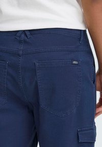 Námornícke modré cargo nohavice vyrobené z odolného materiálu, s klasickým dizajnom, dvoma zadnými vreckami a malou značkovou nálepkou pri páse.