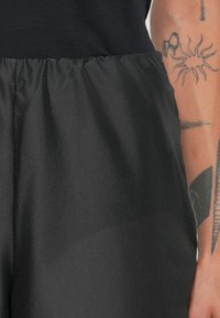 Black shorts with a smooth, shiny texture and an elastic waistband. Close-up view shows lightweight, breathable material.