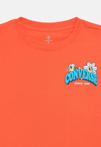 Oransje bomull T-skjorte med rund hals, med blå grafisk tekst "CONVERSE" og tegneserie bier og en blomst. Størrelse S.