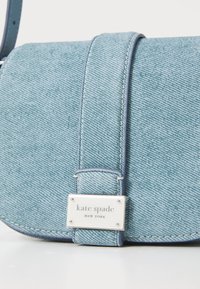 Borsa a tracolla in denim blu chiaro con una texture liscia, dotata di una placchetta con logo argentato e dettagli di cucitura distintivi.