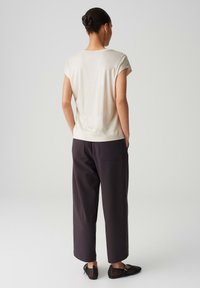Lichtbeige overhemd met korte mouwen in een relaxte pasvorm, gecombineerd met losse donkere broek met achterzakken en platte zwarte schoenen.