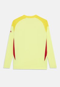 Žlté športové tričko s dlhým rukávom s tmavšími žltými akcentmi na pleciach a červenými bočnými panelmi, zobrazené na flat ležiace s chrbtom smerujúcim dopredu.