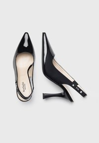 Scarpe con tacco slingback in vernice nera, con punta appuntita, tacchi sottili e borchie decorative sulla cinghia. Superficie liscia e soletta color beige neutro.