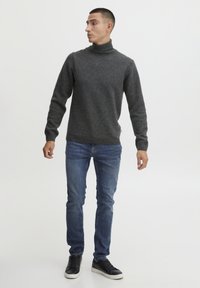 Süsinikmust turtleneck-sviiter, ribitud mansettidega, koos siniste kitsaste teksade ja mustade valge tallaga tossudega. Üksikasjalik taust.