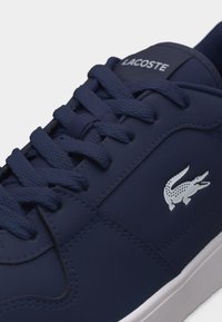 Baskets Lacoste bleu marine avec lacets texturés, logo crocodile blanc sur le côté et semelle en caoutchouc blanche.