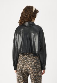 Beskaffet svart faux skinnjakke med spiss krage og lange ermer, samlet med høyreiste bukser med leopardmønster og baklommer.
