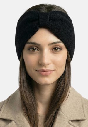 Cinta para la cabeza de forro polar negra con diseño de nudo torcido, textura suave y banda ancha, usada con una prenda exterior beige.