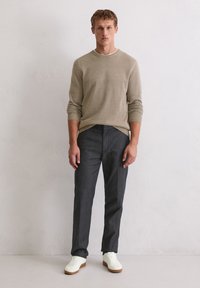 Pull en maille beige avec poignets et col côtelés, associé à un pantalon gris foncé. Le mannequin porte des baskets blanches avec une semelle beige.