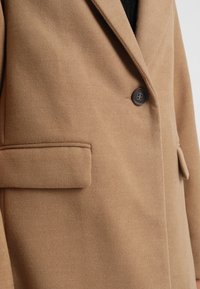 Cappotto in misto lana color sabbia con revers, chiusura a un bottone e tasca laterale, caratterizzato da una morbida texture spazzolata.