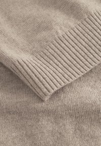 Lys beige strikket sweater med en blød tekstur. Har ribbede manchetter og kant, der viser et glat, ensartet væv over hele stoffet.