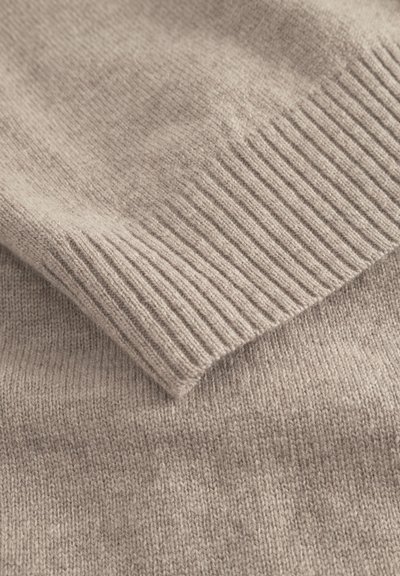 Light beige knit sweater with a soft texture. Features ribbed cuffs and hem, showcasing a smooth, even weave across the fabric.