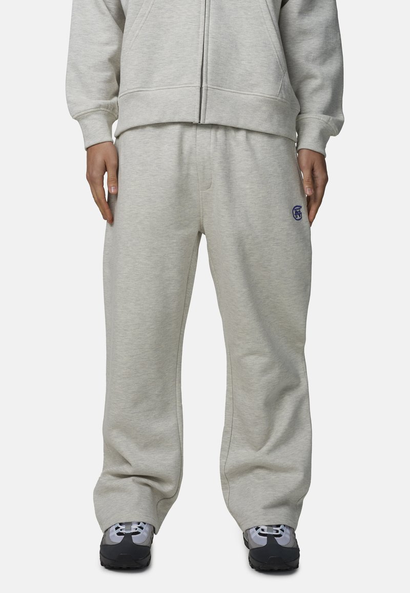 Jasnoszare spodnie dresowe z miękkiego materiału, z wiązanym w pasie sznurkiem, luźnym krojem oraz małym niebieskim logo na lewym biodrze.