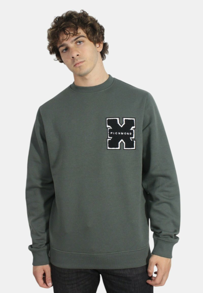 Felpa verde con collo a giro, caratterizzata da un patch ricamato in bianco e nero sul lato sinistro del petto e polsini a coste.