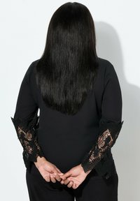 Zwarte top met lange mouwen met ingewikkelde zwarte kanten manchet. Glad materiaal met een slanke silhouette en contrasterende textuuraccenten aan de randen.