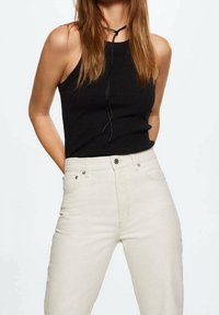 Haut halter en tissu côtelé noir et jeans taille haute beige clair avec poches avant et coutures visibles. Les liens au niveau de l'encolure ajoutent une touche de détail.