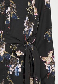 Blusa a maniche lunghe in tessuto nero, con vivaci motivi floreali e di uccelli, dotata di un fiocco in tessuto in vita e dettagli con bottoni.