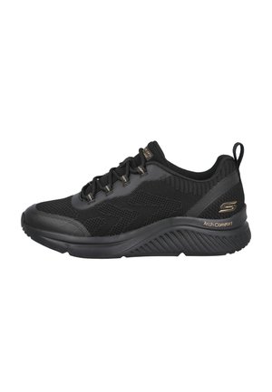 Zapatillas deportivas negras con parte superior de malla, suela acolchada y acentos texturizados. Incluyen cordones negros y una lengüeta trasera para facilitar su uso.