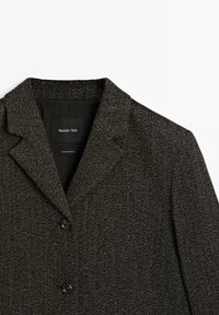 Szary żakiet w wzór rybia łuska z klapami, dwoma czarnymi guzikami i czarną metką wewnątrz. Tkanina ma teksturowany, pleciony wygląd.