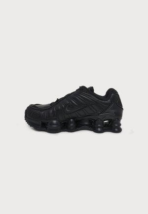 Baskets Nike Shox noires avec tige en cuir, colonnes d'amorti visibles dans la semelle et logo Nike sur le côté, vues du côté extérieur.