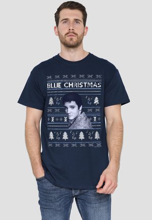 Mann trägt ein marineblaues "Blue Christmas"-T-Shirt mit einem schwarz-weißen Porträt sowie dekorativen Weihnachtsbäumen und Musiknoten.