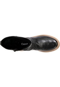 Schwarze Lederstiefelette mit abgerundeter Zehenform und einer tanfarbenen Gummisohle. Sie verfügt über einen seitlichen Reißverschluss für einen einfachen Zugang und ein weiches Innenfutter.