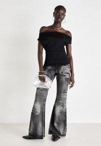 Juodas off-shoulder viršus, nusidėvėję pilki platūs džinsai ir juodos smailianos šlepetės su nagais. Sidabrinė metalinė rankinė ir karoliai.