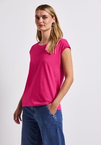 Krátký rukáv růžového trička s kulatým výstřihem a jemnou strukturou, spárovaného s volnými modrými denimovými kalhotami s bočními kapsami.