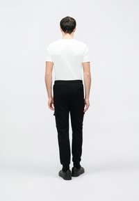 Sorte cargobukser med snøre i taljen, elastiske manchetter og sidelommer, kombineret med en enkel hvid T-shirt med korte ærmer.