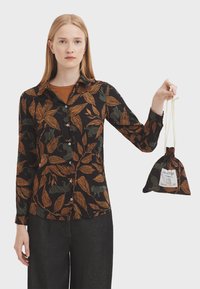 Black button-up shirt with orange and green leaf patterns, paired with a matching drawstring pouch, worn with dark denim pants.