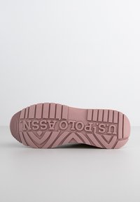 Ljusrosa gummiskosula med ett mönstrat spår. Har varumärket "u.spolo.assn." präglat tydligt på ytan.