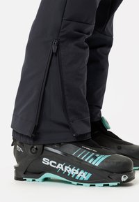 Zwarte skibroek met ritssluitingen aan de onderkant, gecombineerd met zwarte en teal SCARPA skischoenen met een gestructureerde afwerking en duidelijke merknaam.