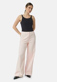 Top nero abbinato a pantaloni ampi rosa chiaro. I pantaloni presentano una texture liscia, un taglio sartoriale e tasche laterali. Scarpe nere a punta.