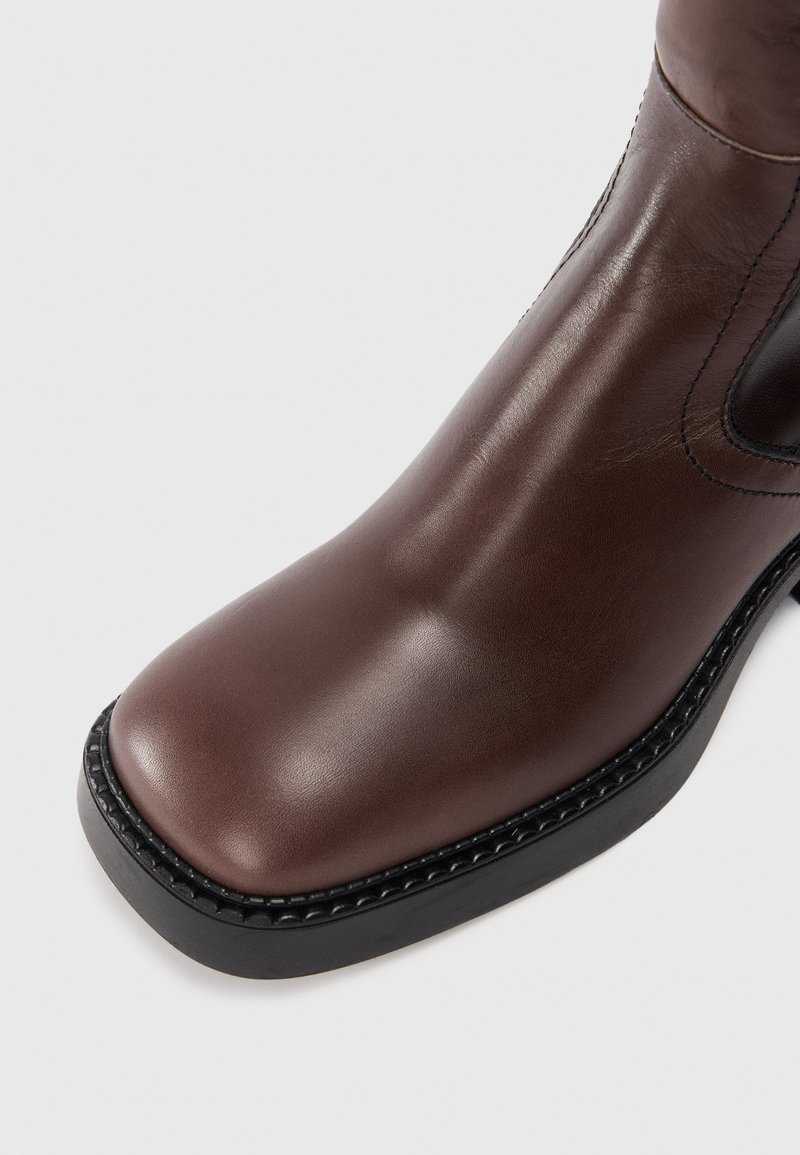 Bottine en cuir marron avec un bout arrondi, texture lisse, semelle noire cousue et panneau élastique latéral pour un meilleur ajustement.