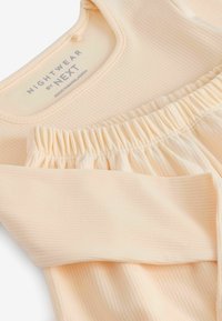 Peach ribbed nightwear top with a rounded neckline and gathered elastic hem. Fabric is soft and smooth, featuring a subtle texture.
