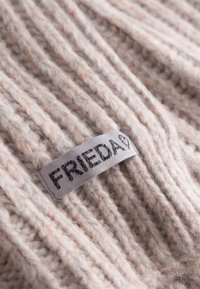 Chunky gebreide trui in lichtbeige met roze vlekken. Voorzien van een grijze stoffen label met "FRIEDA" in zwart erop gedrukt. Gestructureerd, warm en zacht.