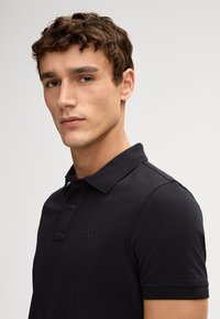 Zwarte polohemd met korte mouwen, gemaakt van zacht materiaal, met een klassieke kraag, een drieknoopsluiting en een subtiele logo op de borst.