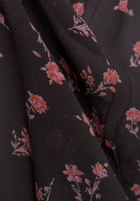 Black fabric with a textured surface features a floral pattern in shades of pink and coral, showing intricate details of petals and stems.