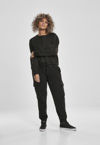Felpa nera con colletto rotondo e maniche lunghe, abbinata a pantaloni cargo neri con tasche laterali. Sneakers nere completano l'outfit.