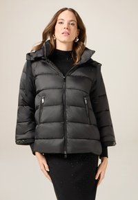 Czarna kurtka puchowa z zamkiem z przodu, dużym kapturem i szerokimi rękawami. Charakteryzuje się pikowaną fakturą i kieszeniami na zamek, skontrastowana z dopasowaną czarną sukienką.