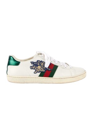 Zapatilla blanca de perfil bajo con rayas verdes y rojas, lengüeta trasera verde, cordones blancos, diseño floral bordado en azul y beige en el lateral.