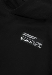 Felpa nera con tessuto a trama. Presenta un'etichetta nera ben visibile con testo bianco: "GARCIAS 1972" e "FONDATA A URBINO ITALIA."