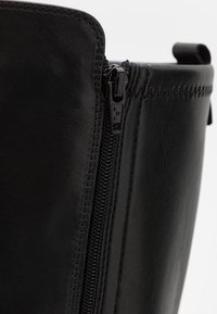 Bottines en cuir noir avec fermeture éclair latérale, texture lisse et couture détaillée le long du bord supérieur.