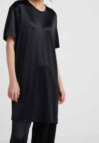 Svart kortärmad klänning i slätt tyg, med rund halsringning, lös passform och en fåll som slutar strax ovanför knäet.