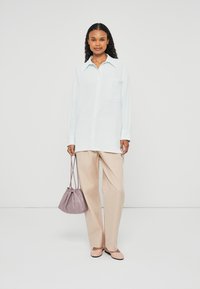 Hellblaues Hemd, beige Hose, hellrosa Ballerinas und eine lavendelfarbene Handtasche. Glatte Texturen und lässiger Schnitt.