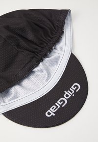 Svart caps laget av lett stoff, med avrundet design, hvite detaljer og en fremtredende logo foran. Teksturert overflate.