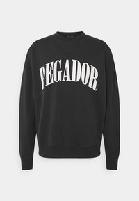 Felpa nera realizzata in morbido tessuto, con la scritta bianca "PEGADOR" in un design arcuato. Polsini e orlo a coste, scollo rotondo.