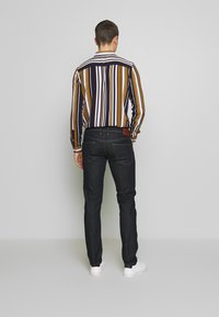 Raidallinen paita tummansinisenä, oranssina ja valkoisena, yhdistettynä tummiin farkkuihin ja valkoisiin tennareihin. Näkymä takaa, jossa näkyy paidan malli ja istuvuus.