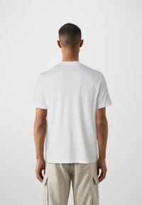 T-shirt blanc à manches courtes en coton avec un col rond, texture lisse et design minimaliste. La vue arrière montre une coupe droite et aucune illustration.