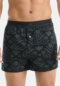 Pantaloni da bagno neri con un motivo floreale tonale, vita elasticizzata con un accento nero e chiusura anteriore con bottone.