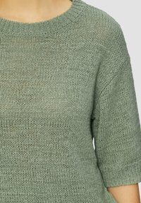 Maglione verde lavorato a maglia con scollatura rotonda, maniche corte e una trama morbida. Il tessuto mostra una leggera trasparenza e una vestibilità rilassata.